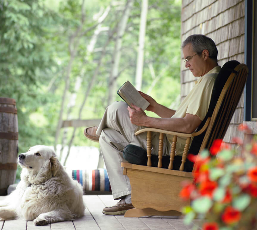 Man sits in chair reading with dog by his side